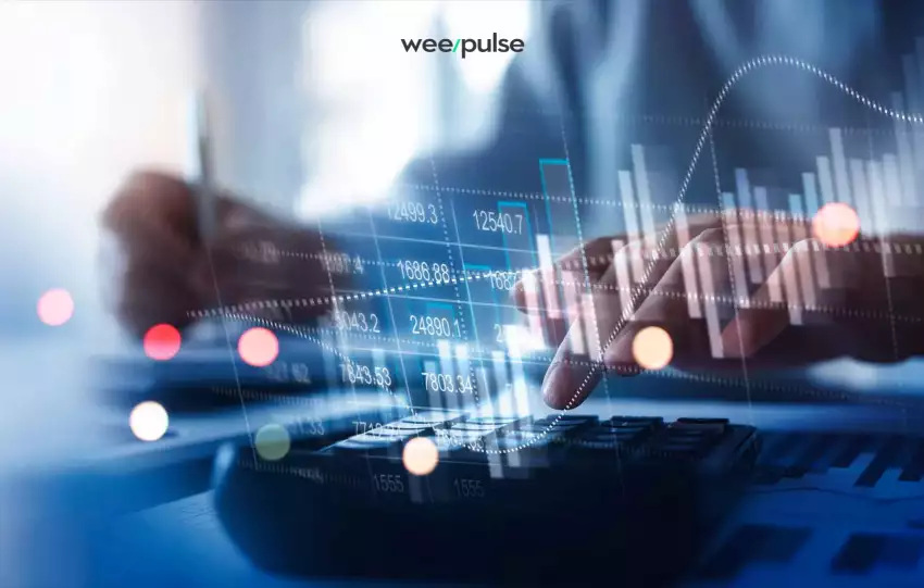 mão esquerda feminina branca utilizando o teclado do computador enquanto a mão direita anota informações financeiros. Na tela há diversos números como uma planilha.